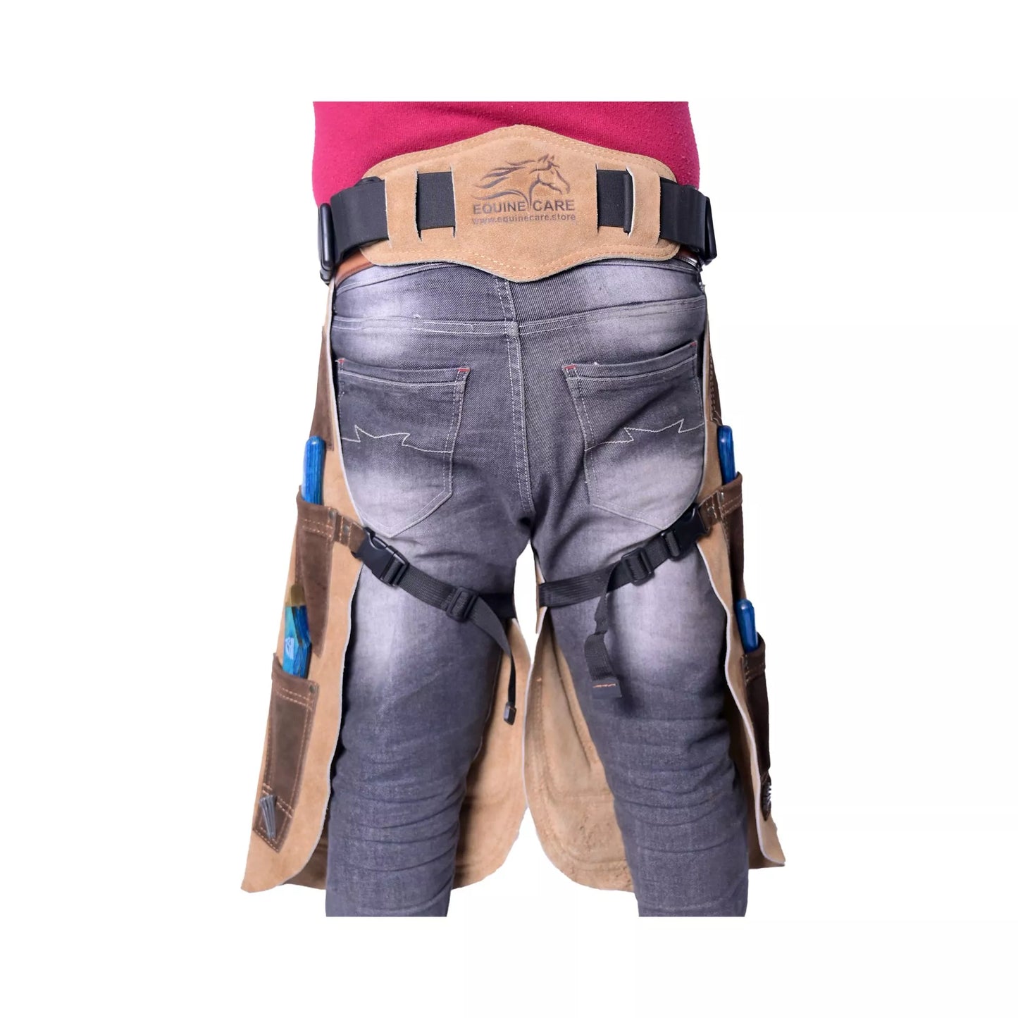 Rear view of brown leather farrier chaps worn over jeans, showing adjustable waist belt, leg straps, and side tool pockets for professional horse shoeing and farrier work